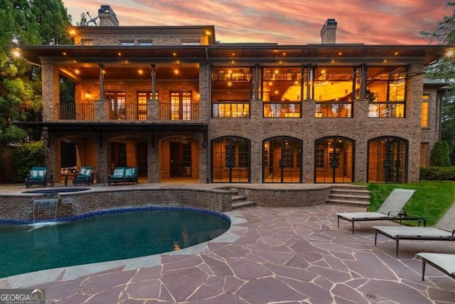 back house at dusk with a patio area, a balcony, and a swimming pool with hot tub