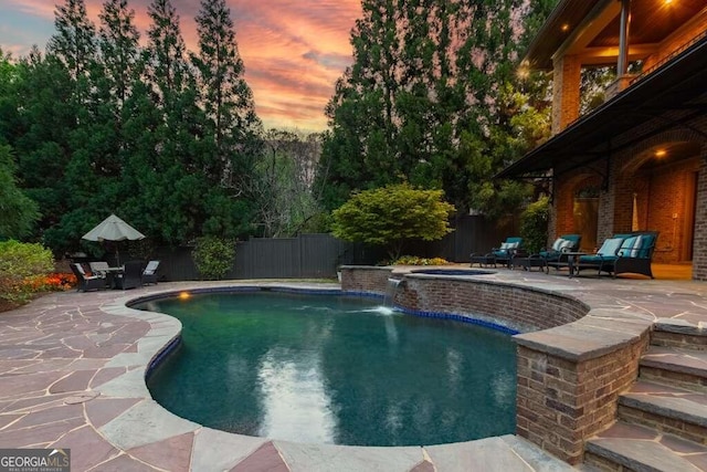 pool at dusk featuring a patio, pool water feature, and an in ground hot tub