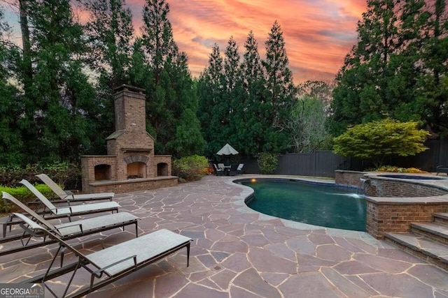 pool at dusk featuring pool water feature, a patio area, an in ground hot tub, and exterior fireplace