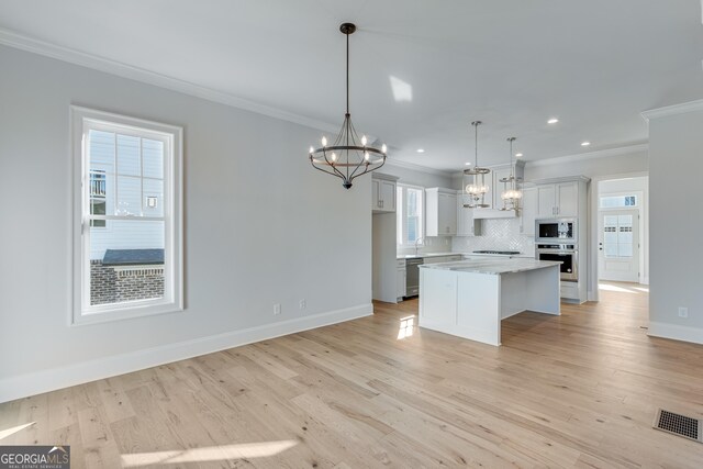 kitchen featuring pendant lighting, a center island, light wood-type flooring, appliances with stainless steel finishes, and light stone counters