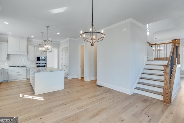 kitchen featuring hanging light fixtures, light wood-type flooring, a kitchen island, white cabinetry, and stainless steel appliances