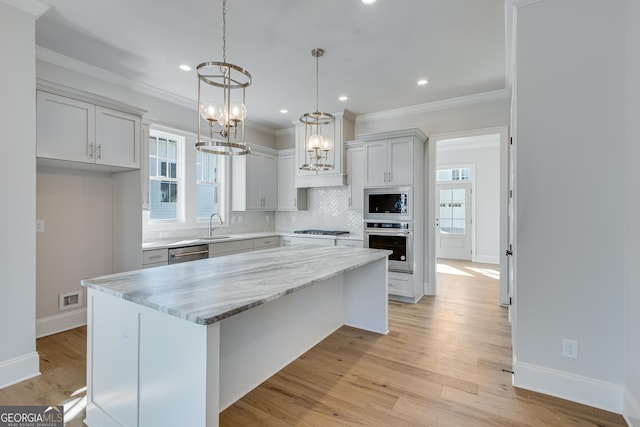 kitchen with appliances with stainless steel finishes, light wood-type flooring, light stone counters, pendant lighting, and a center island