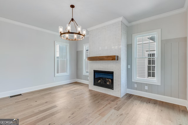 unfurnished living room with a notable chandelier, light hardwood / wood-style floors, ornamental molding, and a brick fireplace