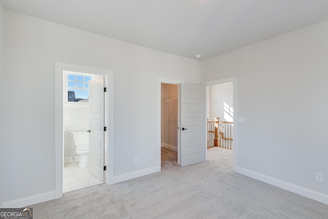 unfurnished bedroom featuring ensuite bath, a spacious closet, a closet, and light colored carpet