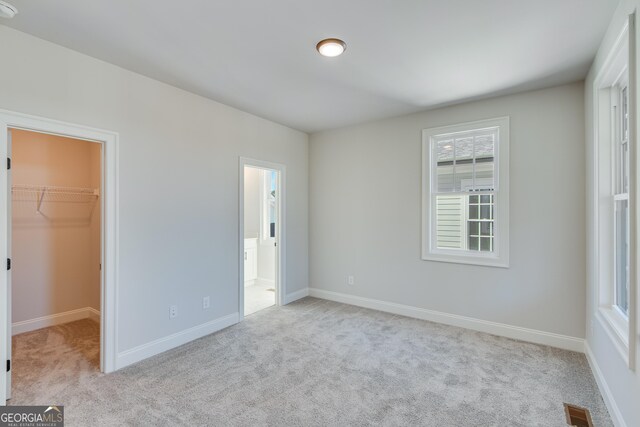 unfurnished bedroom featuring a walk in closet, light colored carpet, ensuite bath, and a closet