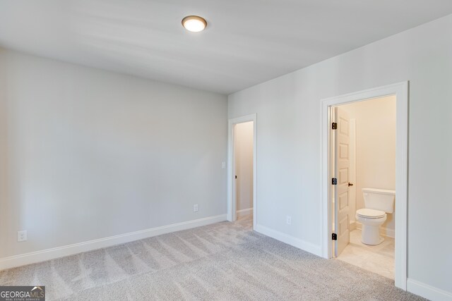 unfurnished bedroom featuring light carpet and connected bathroom