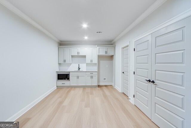 kitchen featuring stainless steel microwave, sink, crown molding, light hardwood / wood-style floors, and white cabinetry