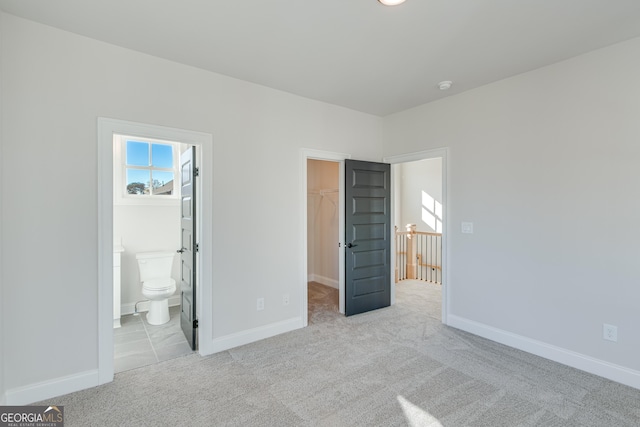 unfurnished bedroom featuring light colored carpet, a spacious closet, a closet, and ensuite bathroom