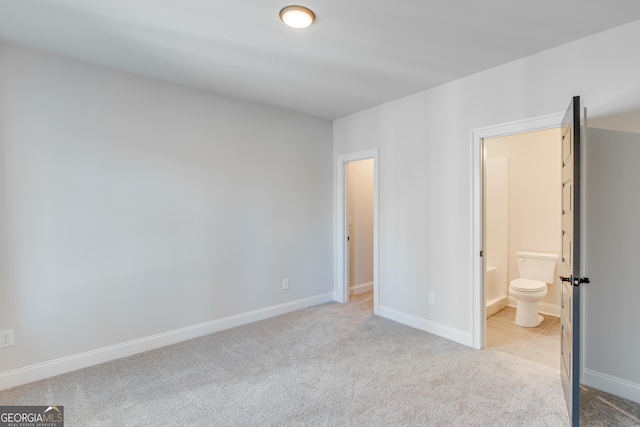 unfurnished bedroom featuring light carpet and ensuite bathroom