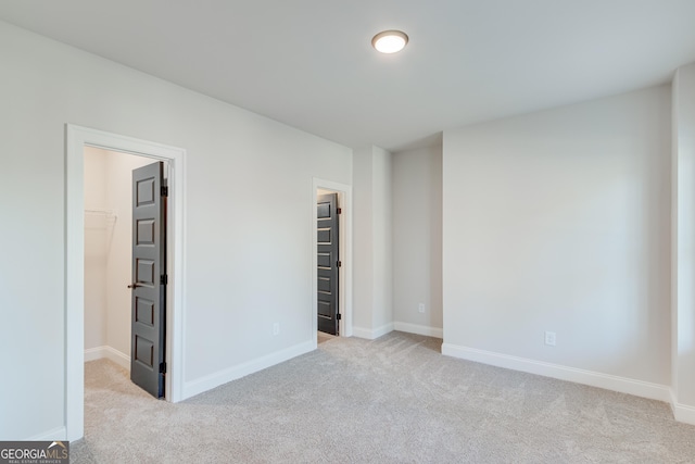 unfurnished bedroom featuring a spacious closet, a closet, and light carpet