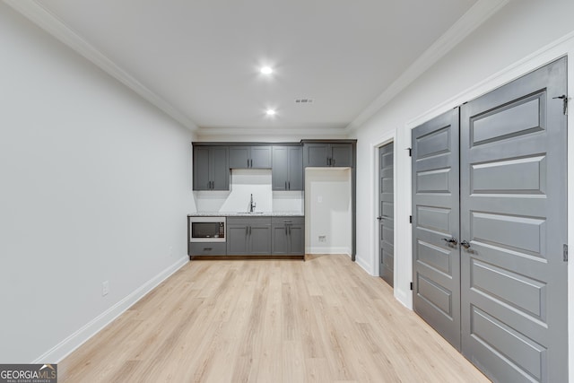 kitchen featuring stainless steel microwave, sink, gray cabinets, ornamental molding, and light hardwood / wood-style floors