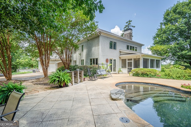 rear view of house featuring a sunroom, a garage, and a patio area