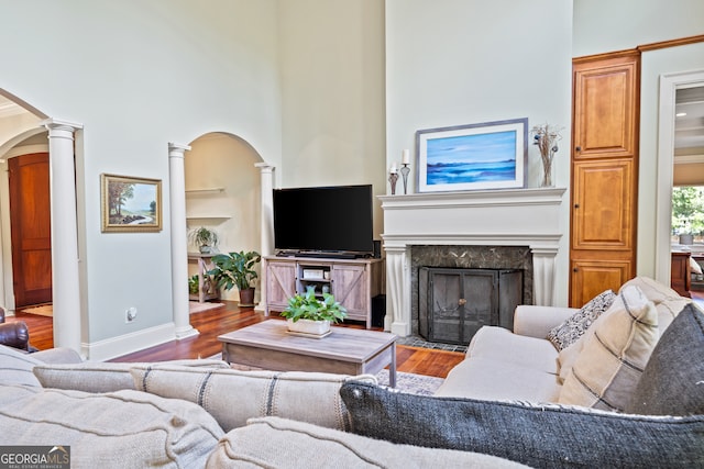 living room with a high end fireplace, hardwood / wood-style flooring, ornate columns, and a towering ceiling