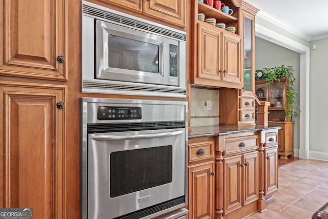 kitchen featuring tasteful backsplash, crown molding, dark stone countertops, appliances with stainless steel finishes, and light tile patterned floors