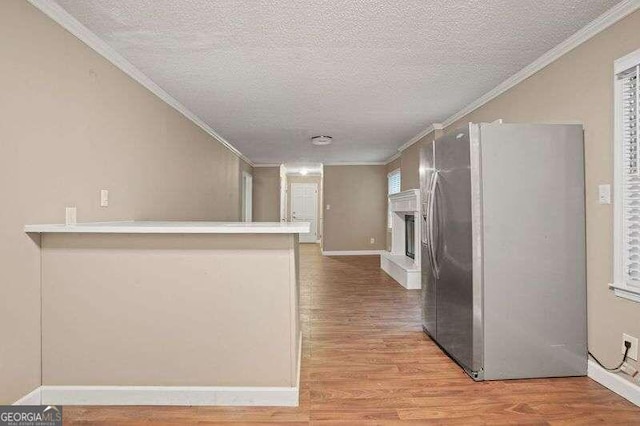 kitchen featuring stainless steel fridge with ice dispenser, kitchen peninsula, wood-type flooring, a textured ceiling, and ornamental molding