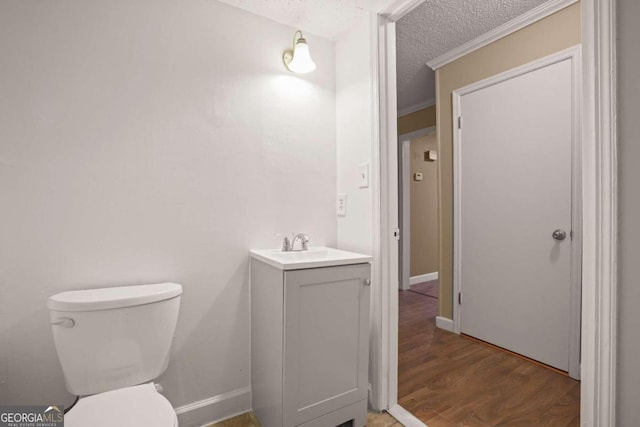 bathroom featuring a textured ceiling, vanity, toilet, ornamental molding, and hardwood / wood-style flooring