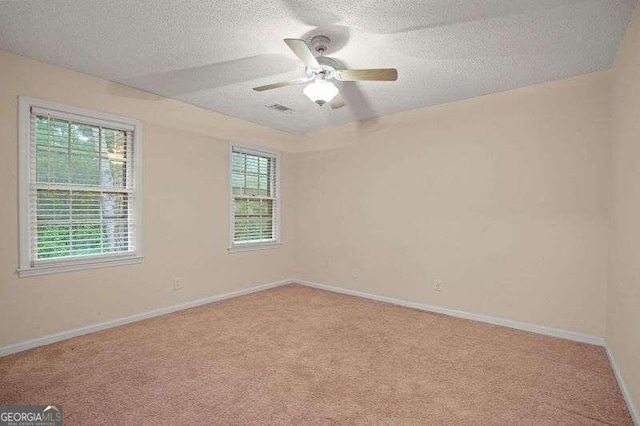 empty room with ceiling fan, light colored carpet, and a textured ceiling