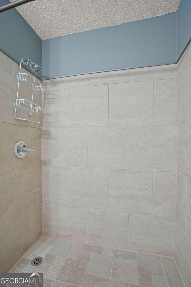 bathroom with a textured ceiling and tiled shower