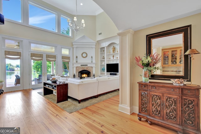 living room with a towering ceiling, a chandelier, plenty of natural light, and light wood-type flooring