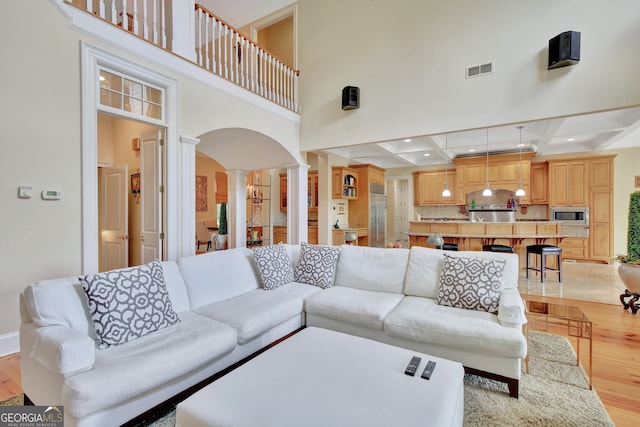 living room with light hardwood / wood-style flooring, ornate columns, coffered ceiling, and a high ceiling