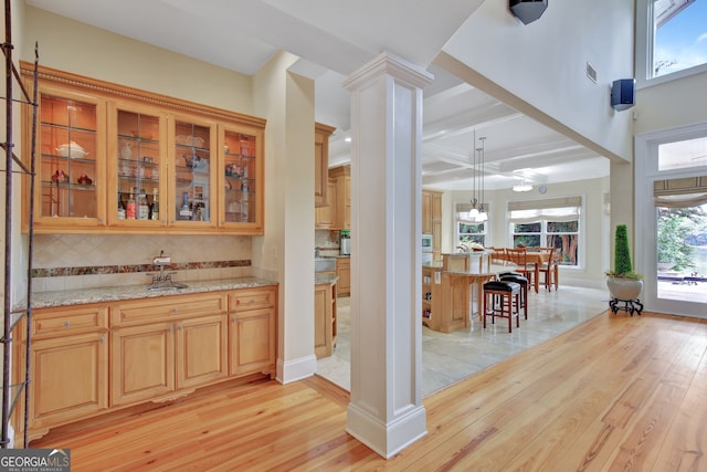 kitchen with beamed ceiling, light hardwood / wood-style flooring, decorative columns, light stone counters, and tasteful backsplash