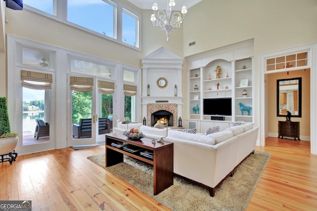 living room with light hardwood / wood-style floors, a towering ceiling, an inviting chandelier, and built in shelves