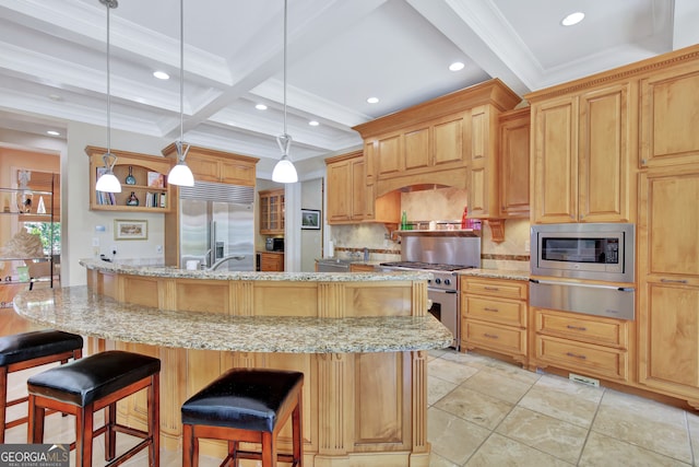 kitchen featuring a kitchen island with sink, a kitchen bar, beamed ceiling, built in appliances, and decorative light fixtures