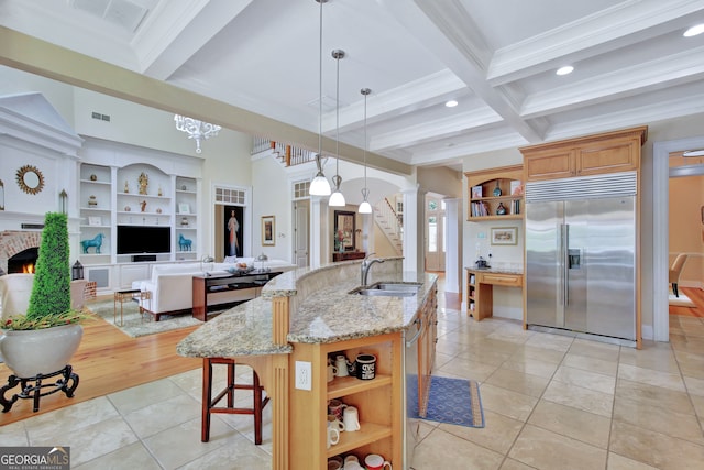 kitchen featuring a center island with sink, hanging light fixtures, sink, built in fridge, and light stone counters