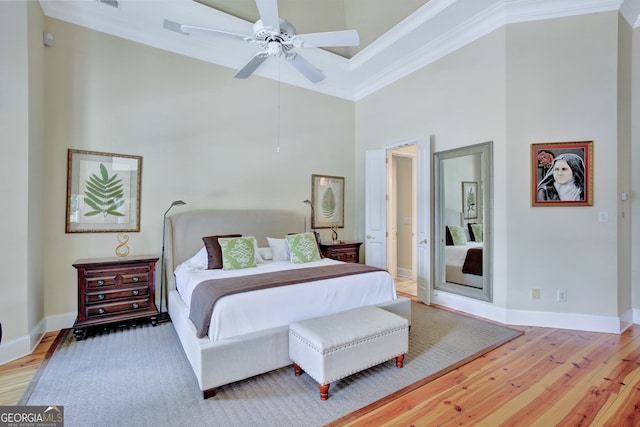 bedroom with ceiling fan, crown molding, a high ceiling, and light wood-type flooring