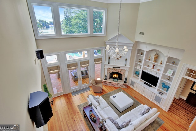 living room featuring a towering ceiling, a fireplace, hardwood / wood-style floors, crown molding, and an inviting chandelier