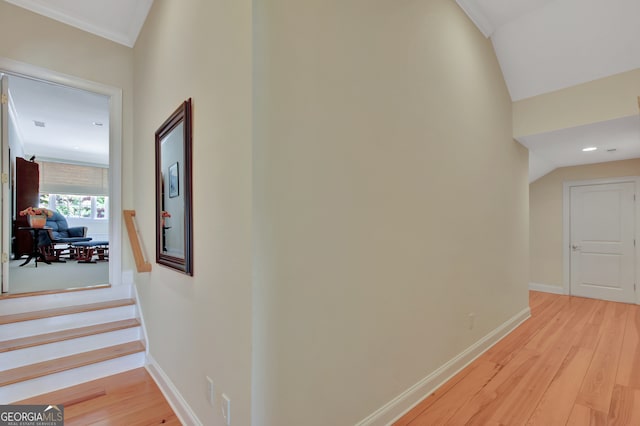 hallway with light hardwood / wood-style floors, lofted ceiling, and ornamental molding