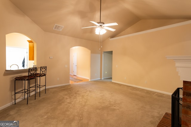 living room featuring carpet, a brick fireplace, ornamental molding, vaulted ceiling, and ceiling fan