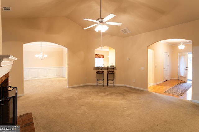 unfurnished living room with light carpet, a fireplace, high vaulted ceiling, and ceiling fan with notable chandelier