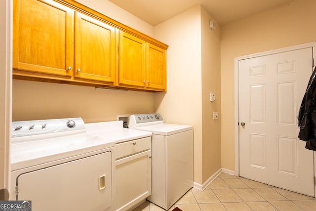 clothes washing area featuring washer and dryer, light tile patterned flooring, and cabinets