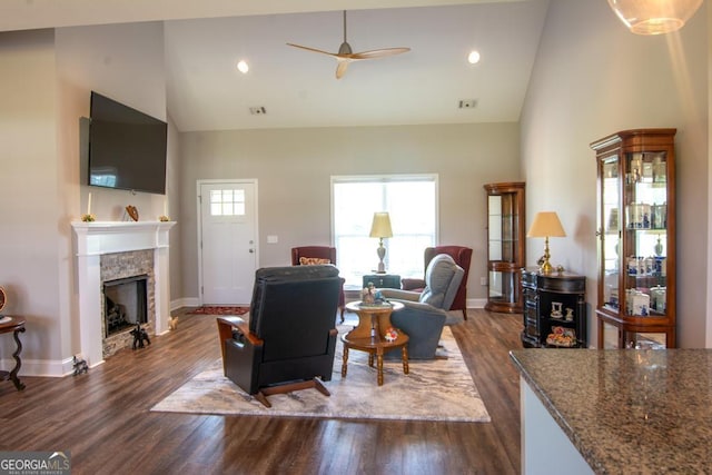 living room featuring a stone fireplace, dark wood-type flooring, ceiling fan, and high vaulted ceiling