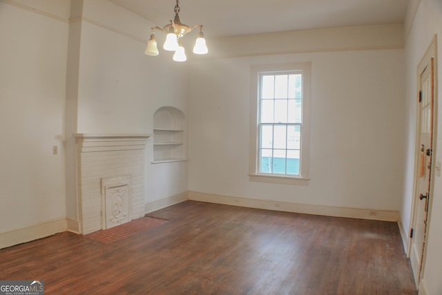 unfurnished living room with dark hardwood / wood-style flooring, a brick fireplace, a notable chandelier, and built in features