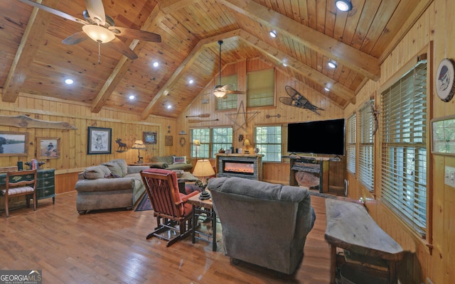 living area with ceiling fan, a glass covered fireplace, wood-type flooring, and wooden walls