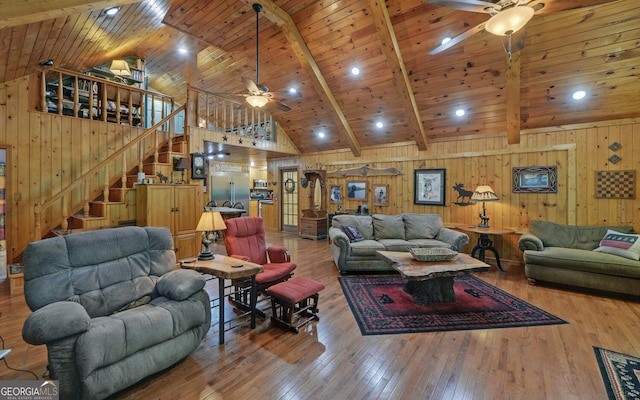 living area with stairway, wood-type flooring, a ceiling fan, and wooden walls