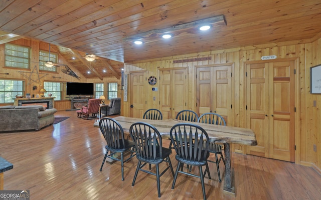 dining area with high vaulted ceiling, light hardwood / wood-style flooring, wooden ceiling, wooden walls, and ceiling fan