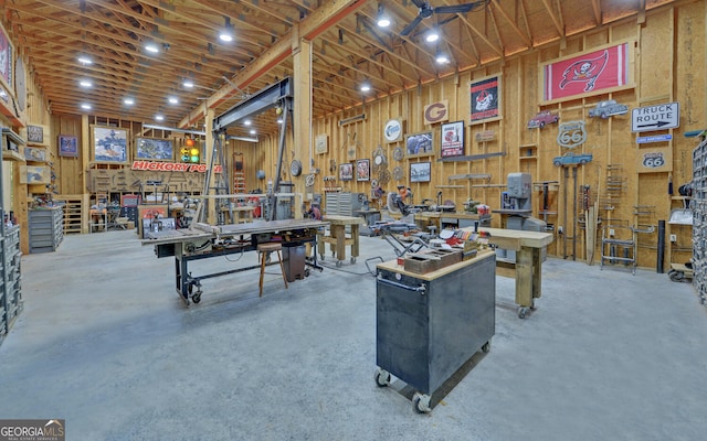 miscellaneous room with a workshop area, concrete floors, and wooden walls