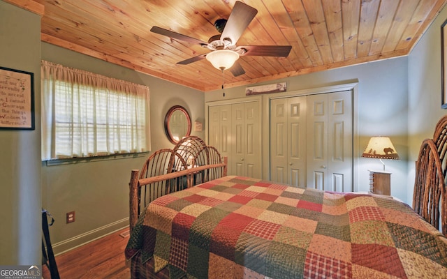 bedroom with wood ceiling, dark hardwood / wood-style floors, ceiling fan, and two closets