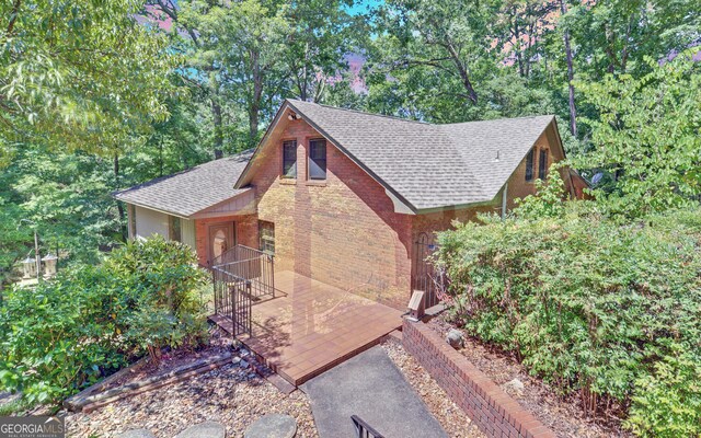 view of side of home with roof with shingles and brick siding