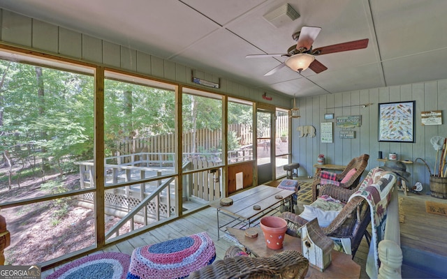 sunroom / solarium with hardwood / wood-style floors, a ceiling fan, wood walls, and an outdoor living space