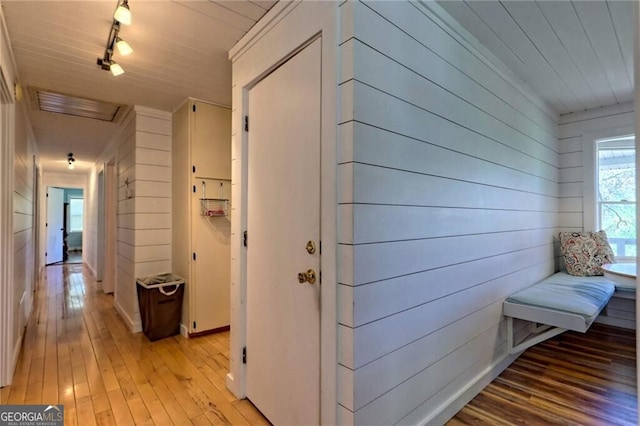 hallway with track lighting, light hardwood / wood-style floors, and wooden walls