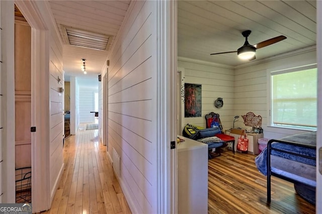 corridor with crown molding, wood walls, and light wood-type flooring