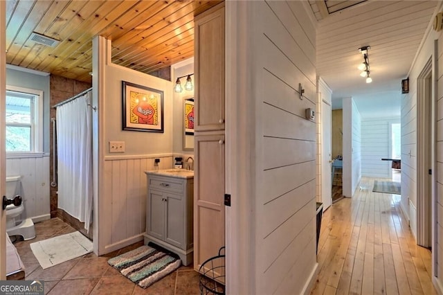 bathroom featuring wood walls, wooden ceiling, track lighting, vanity, and curtained shower