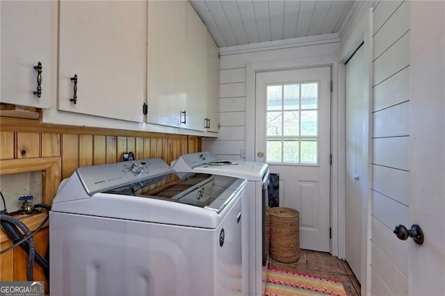 laundry area with light tile patterned flooring, washer and dryer, wooden walls, and cabinets