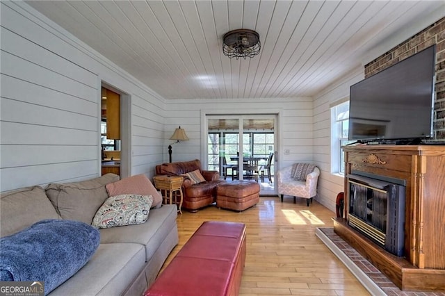 living room featuring light hardwood / wood-style floors, wooden ceiling, a large fireplace, and wooden walls