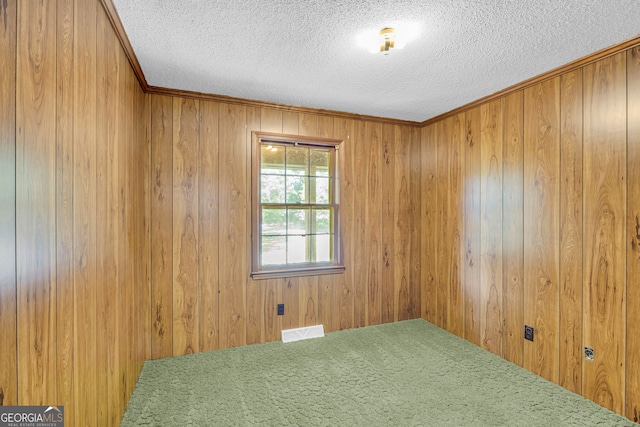 unfurnished room with a textured ceiling, crown molding, and wood walls