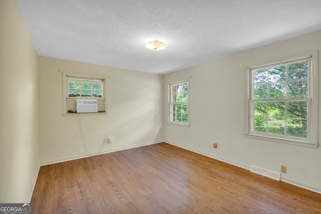 unfurnished room with plenty of natural light, cooling unit, light hardwood / wood-style floors, and a textured ceiling